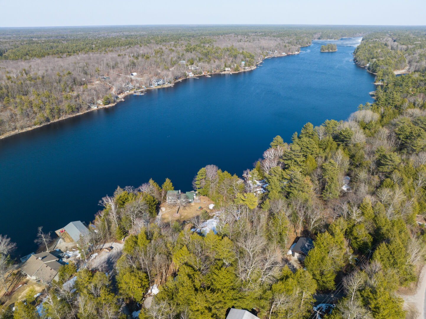A long, narrow stretch of lake. Green trees and large cottages line the shore on either side.