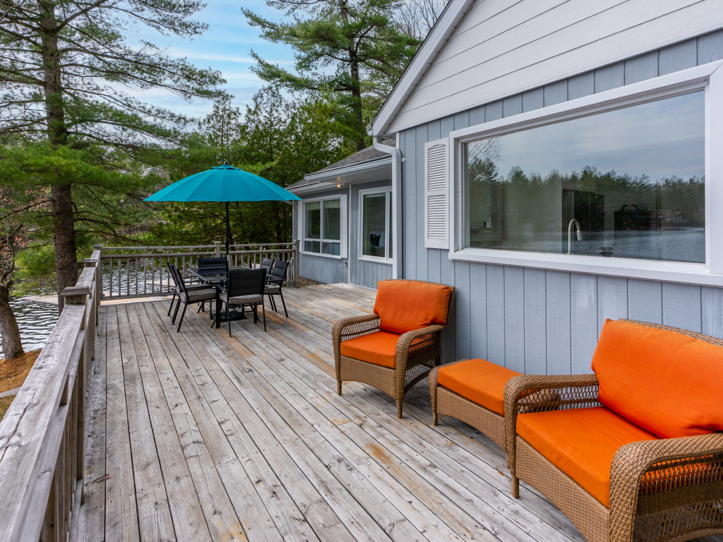 A deck with orange patio furniture and a green umbrella extends off the back of a cottage, which has a large window.