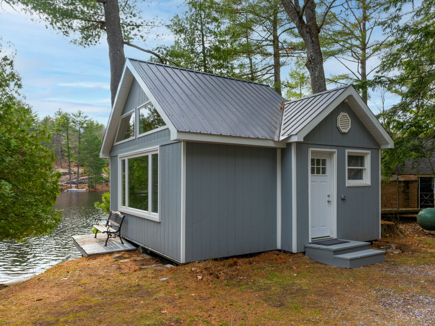 Exterior of a small lakeside bunkie with a big window and a white door,