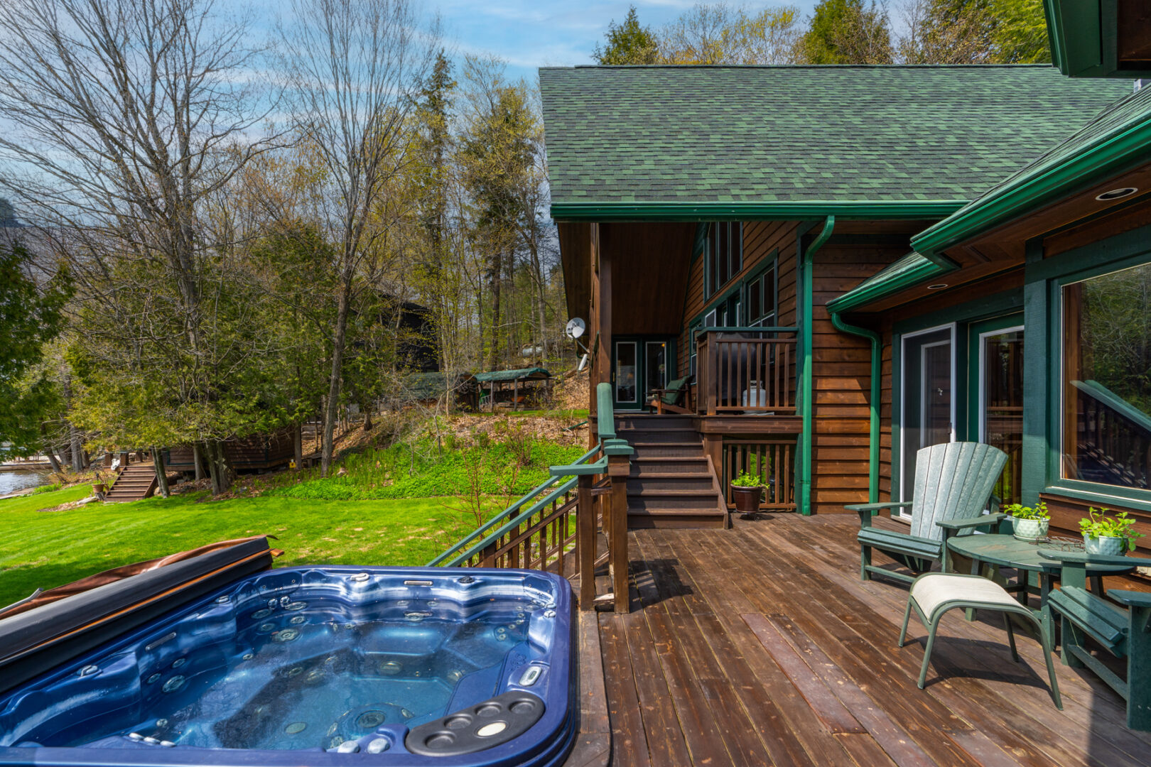 A large deck extending off the back of a cottage, with a hot tub set down in line with the dark wood deck floor.