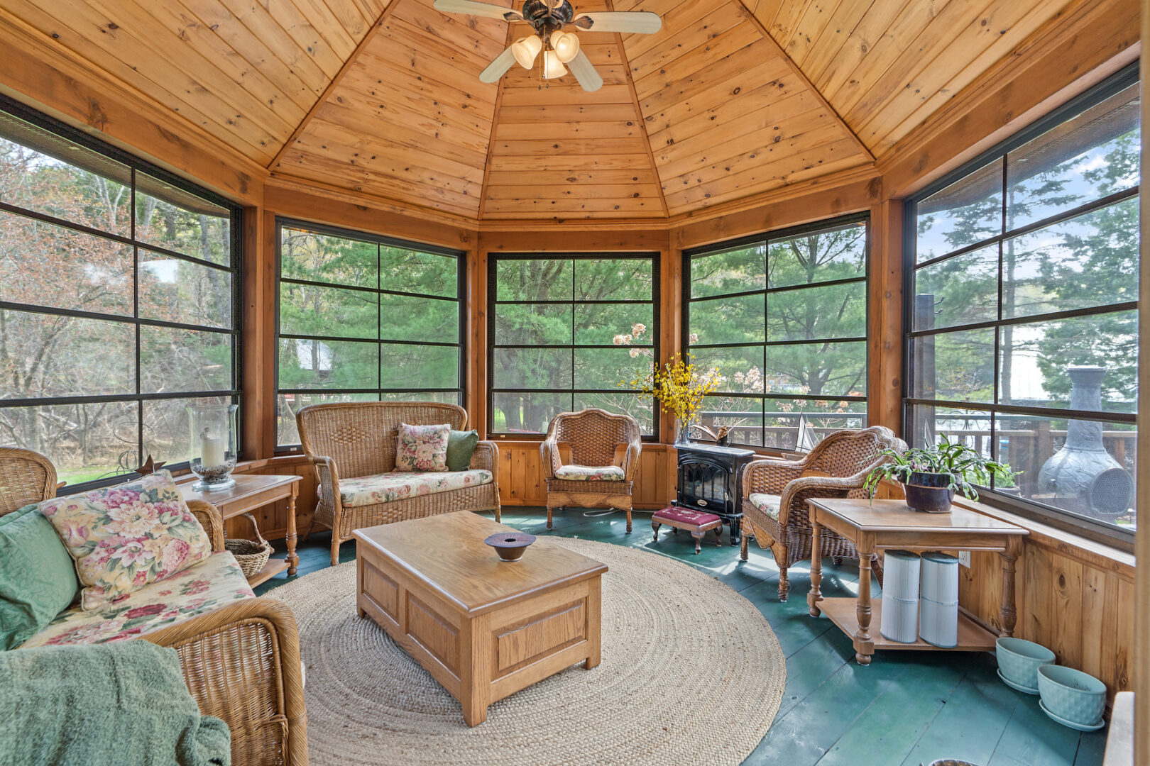 Interior of an octagonal screened-in room with tons of seating, a wood-panelled ceiling, and a ceiling fan.