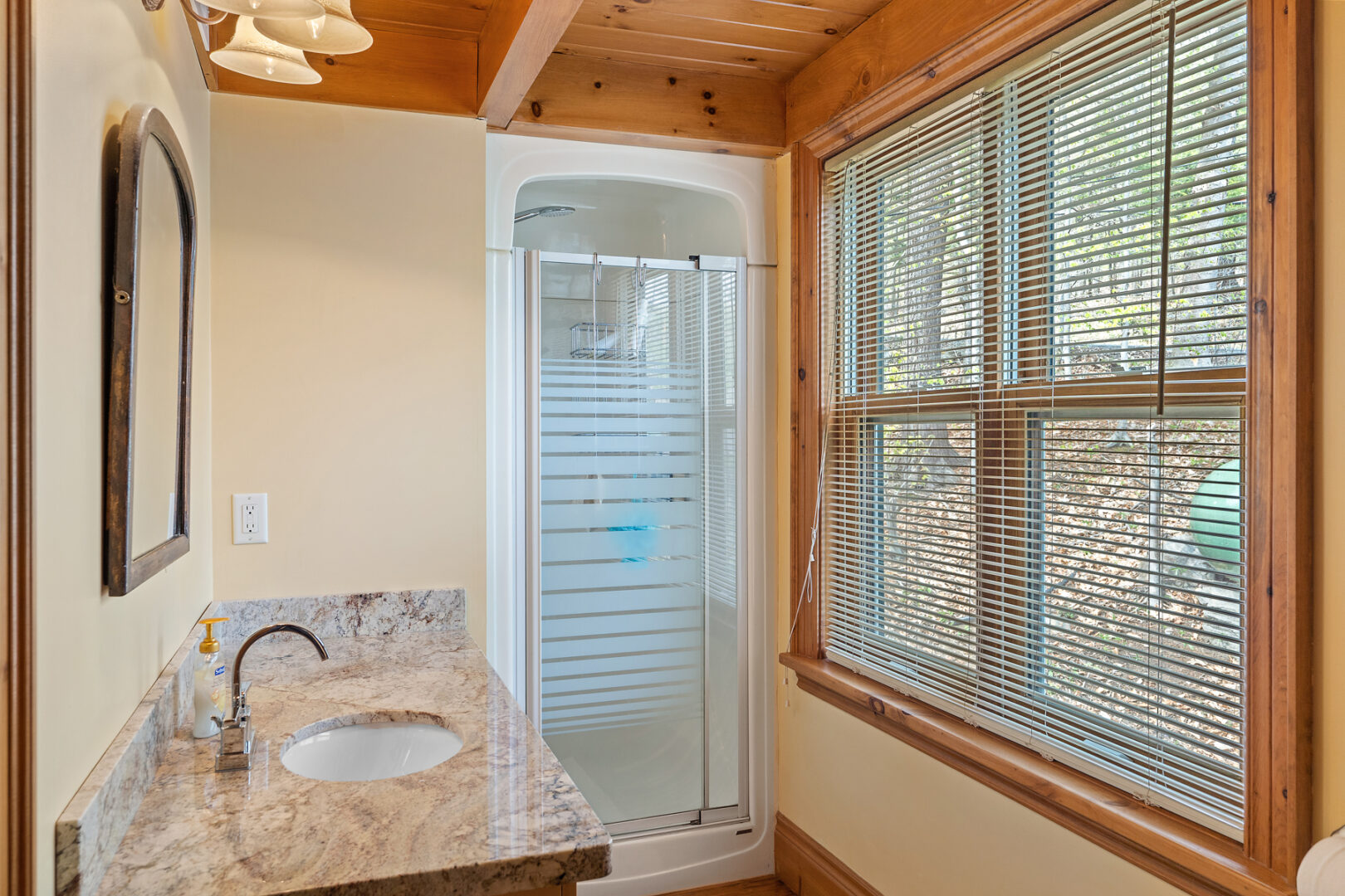 A bathroom with a small walk-in shower, a sink, and a big window.