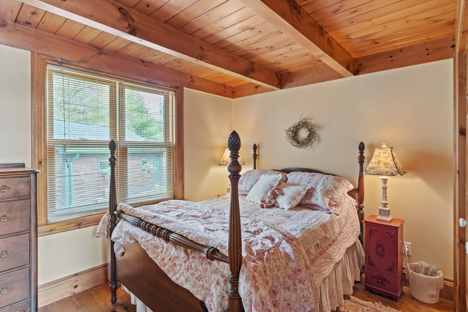 A small bedroom with a large four-posted bed, a wood-panelled ceiling, and a big window.