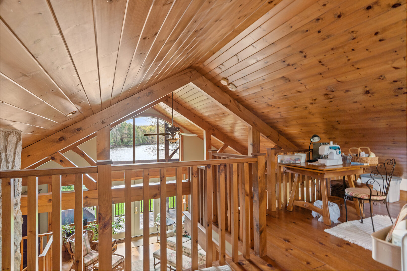 A loft space looking out over a lower level of the house, with slanted wood-panelled ceiling a wooden railing.