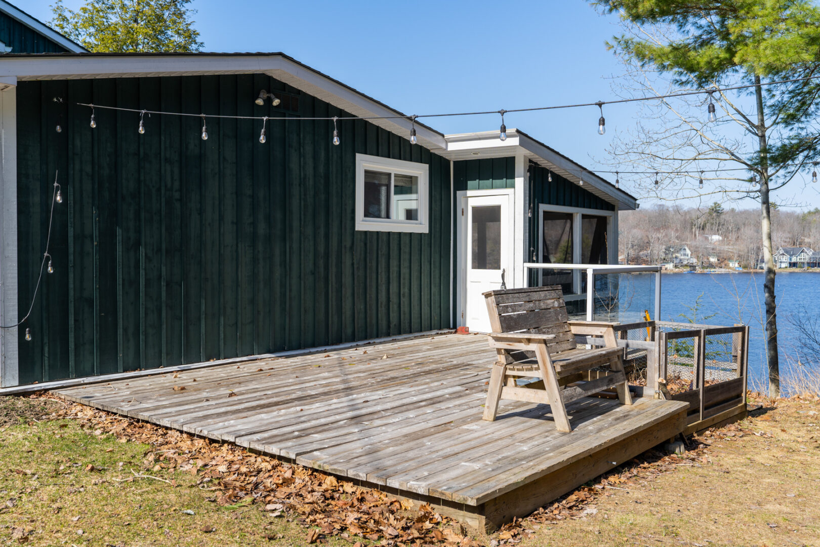 A wooden deck extends off the side of a green cottage. String lights hang suspended overhead.
