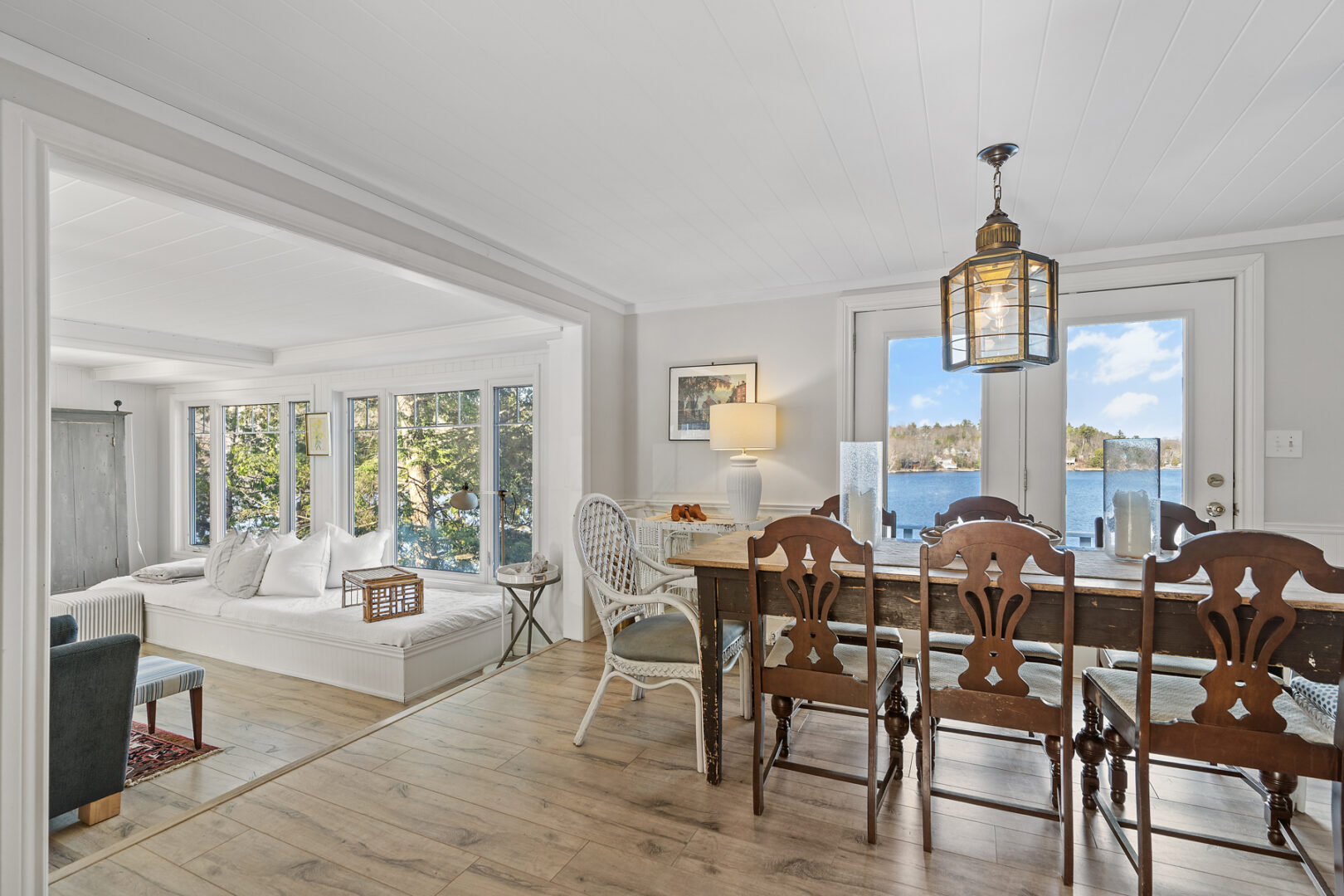 An open-concept cottage living space with a dining area, a window seat, and large windows overlooking lake views.