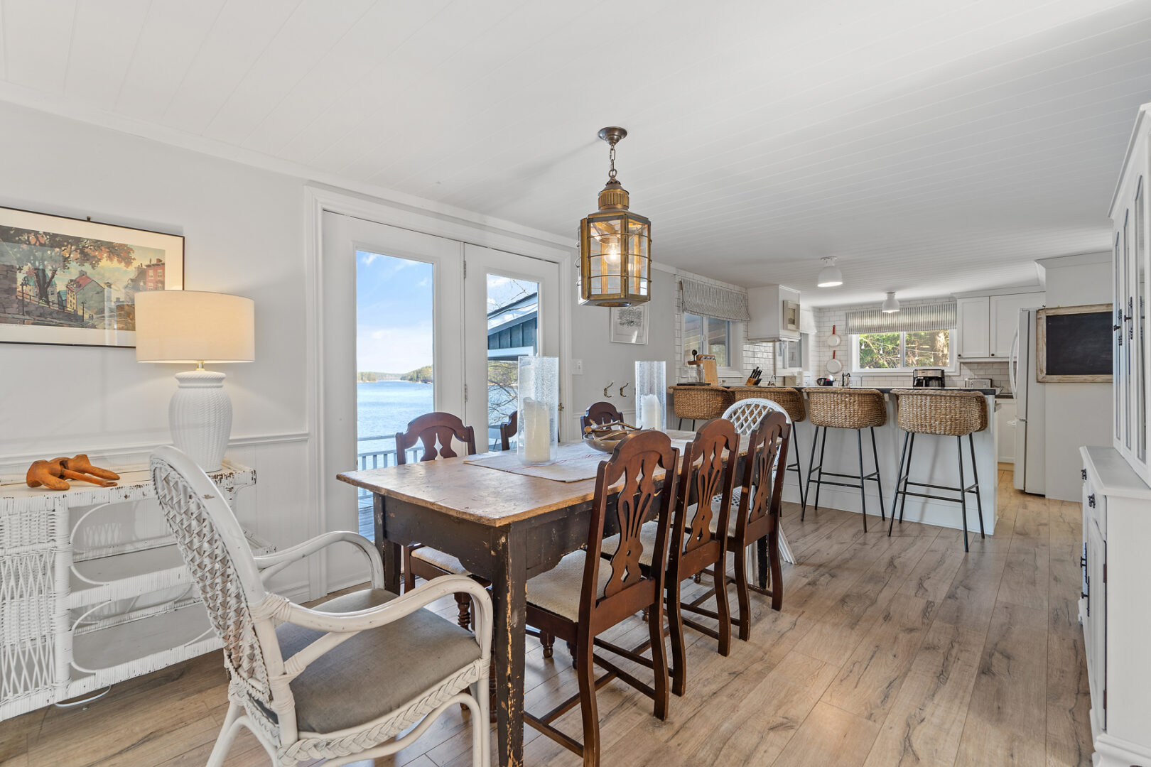 A bright interior space with a dining table, chairs, and large windows offering a lake view.