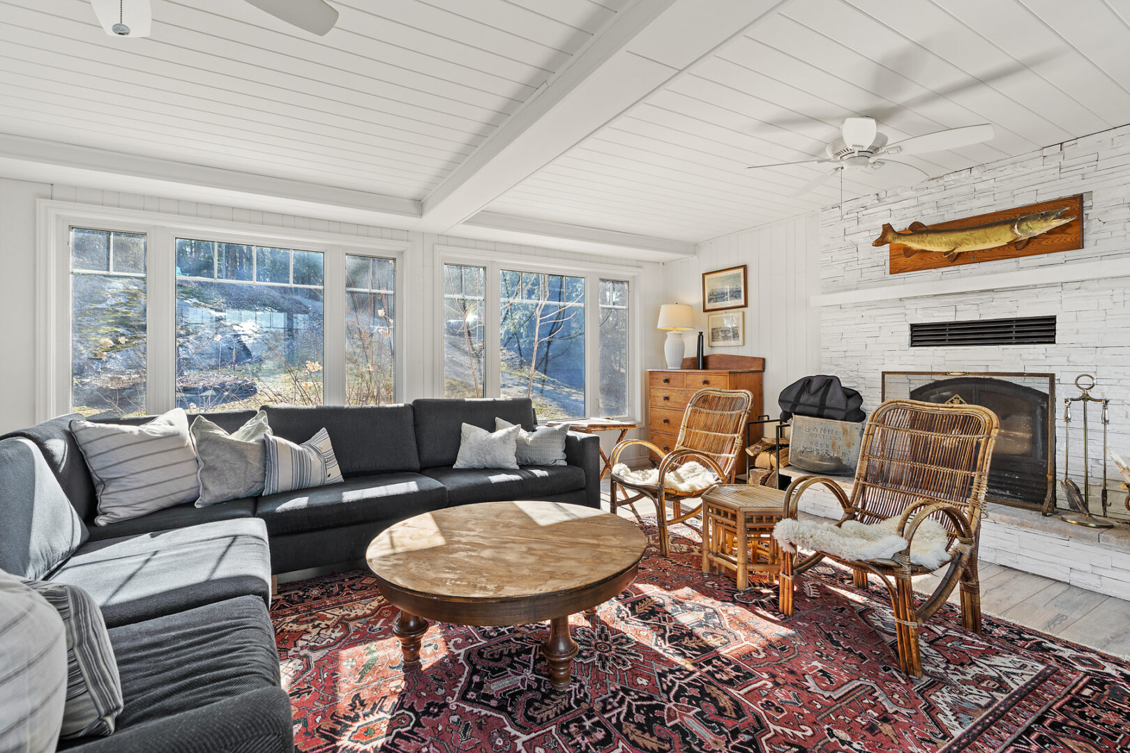 A large cottage, bright living area with a couch, an ornate rug, a coffee table, and large windows.