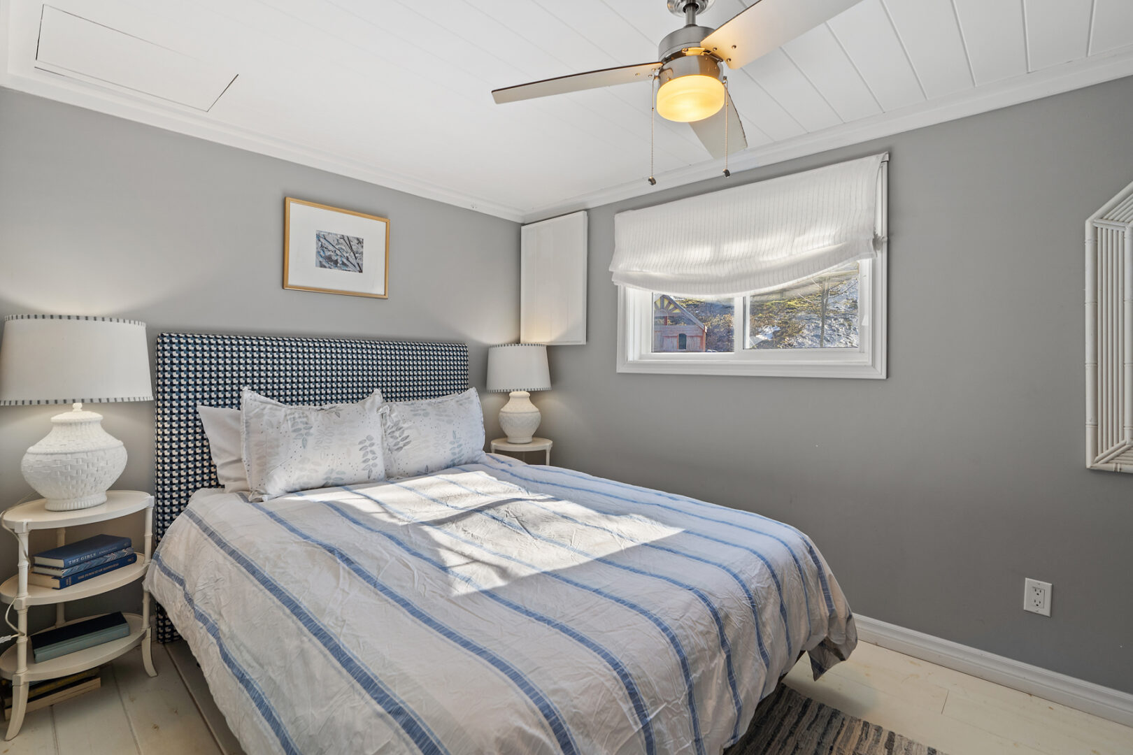 A big bedroom with a large bed, a window, a ceiling fan, and gray walls.