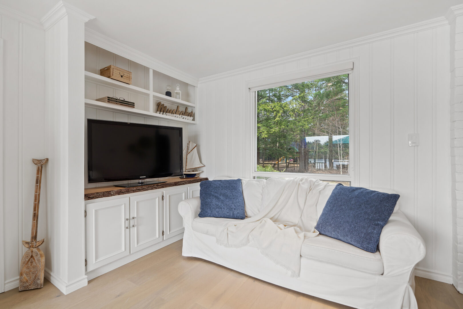 A small white couch sits against a wall with a window, close to a television.