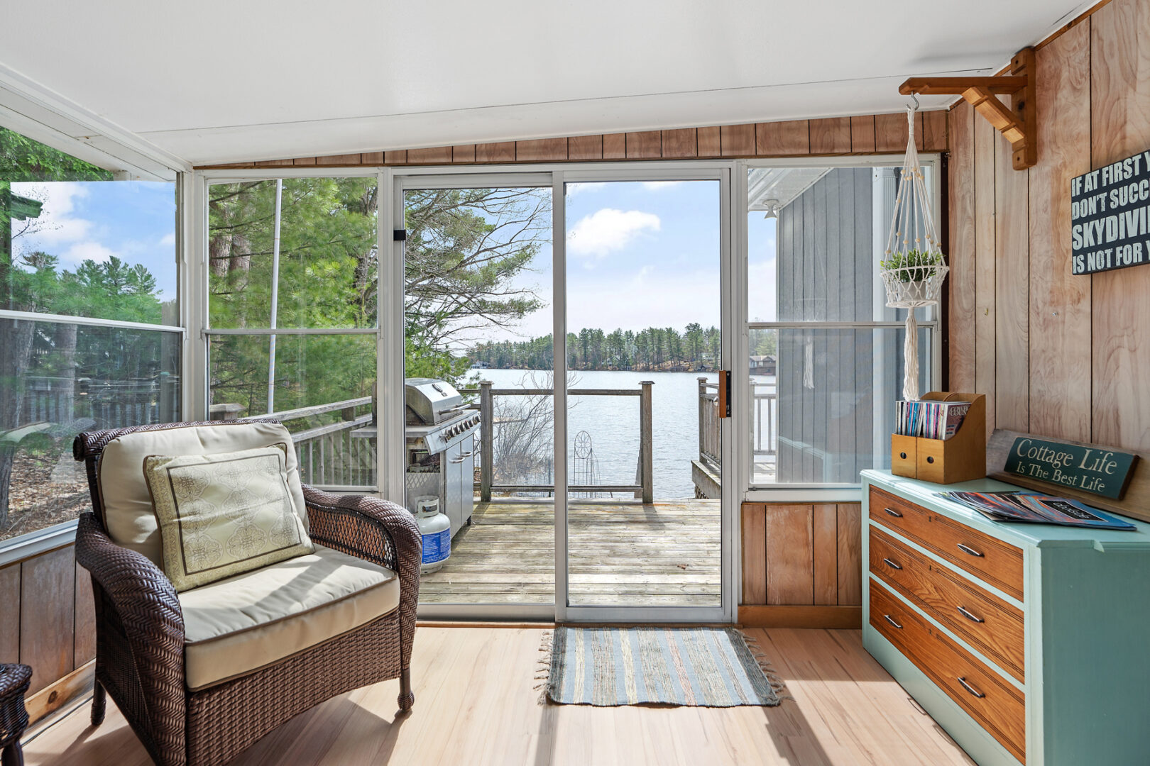 A bright sunroom with a chair and large windows all around. A lake view can be seen through the doorway.