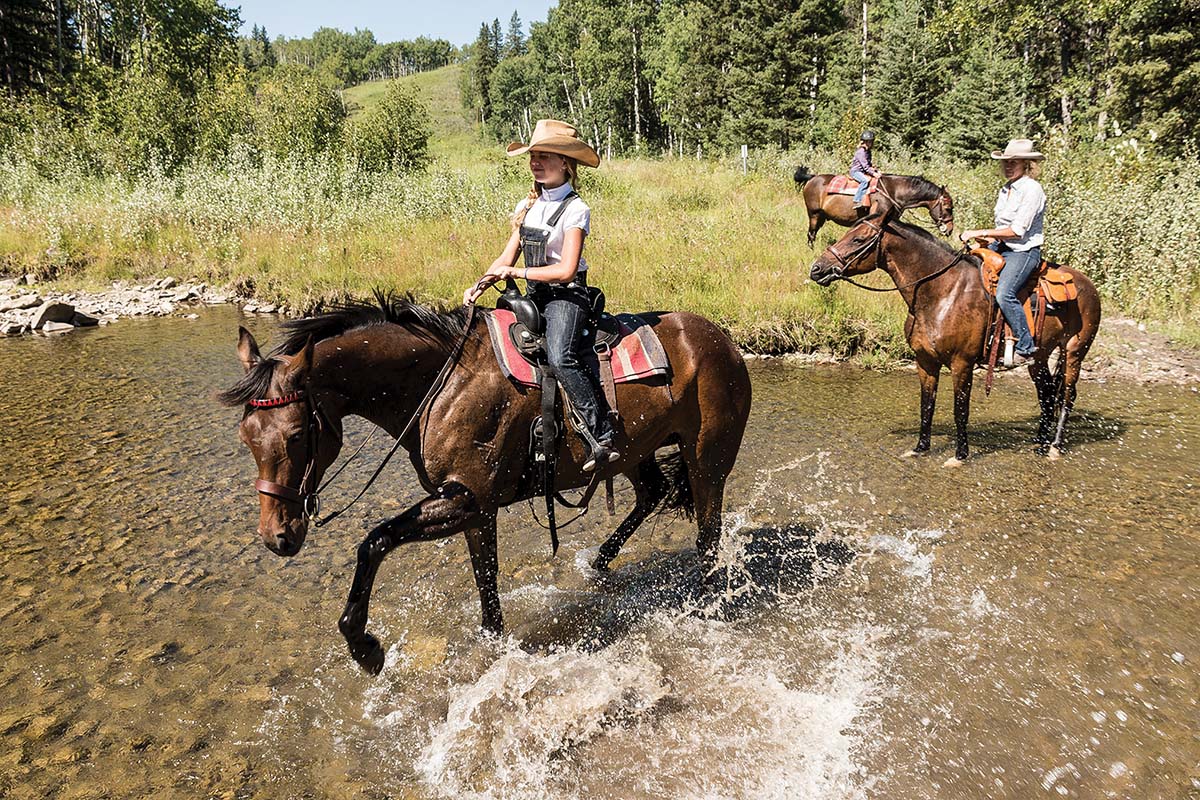 Levi, Cathy, and Jessie ride horses through Threepoint creek