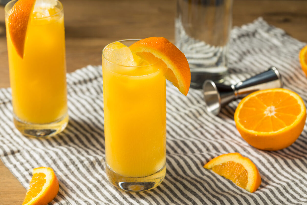 Two screwdriver cocktails with orange slices sitting on striped cloth