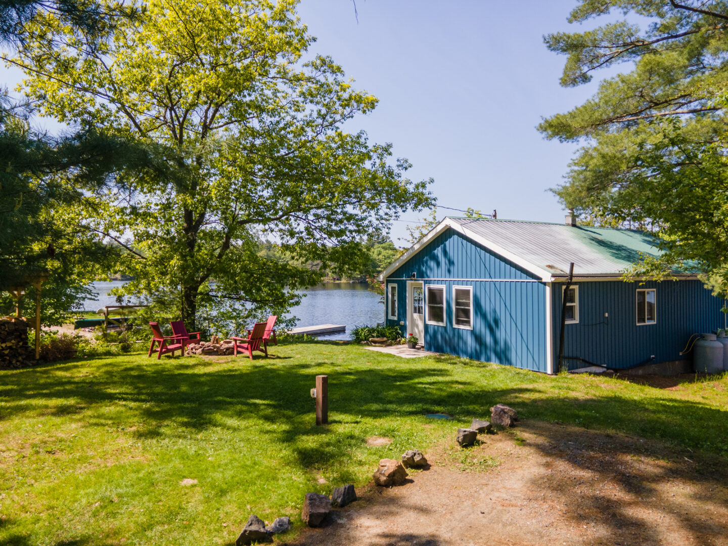 A small blue cottage sits behind a wide green lawn, in front of a blue lake.