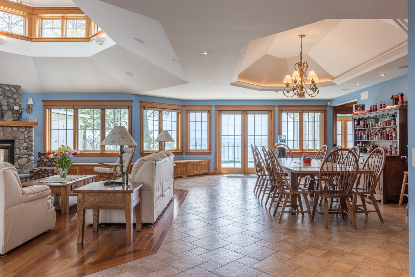 A bright, open-concept living and dining area in a large lake house, with lots of windows and hardwood floors.