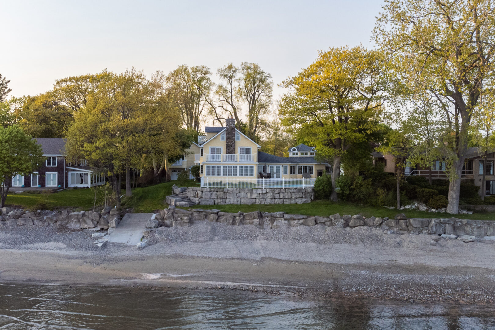 A large lake house sits just up the shore of a sandy lakeside beach.