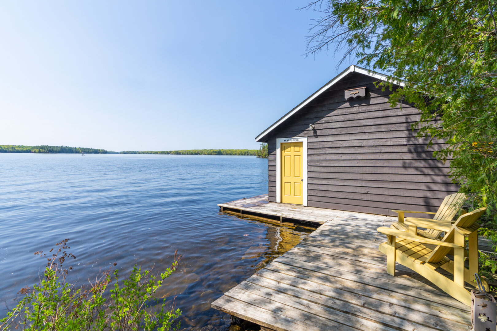 A big boathouse sits just off a stretch of dock on a lake shoreline.