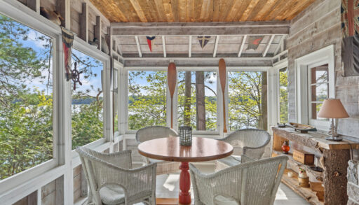 A bright cottage sunroom with white deck flooring and white wicker furniture.