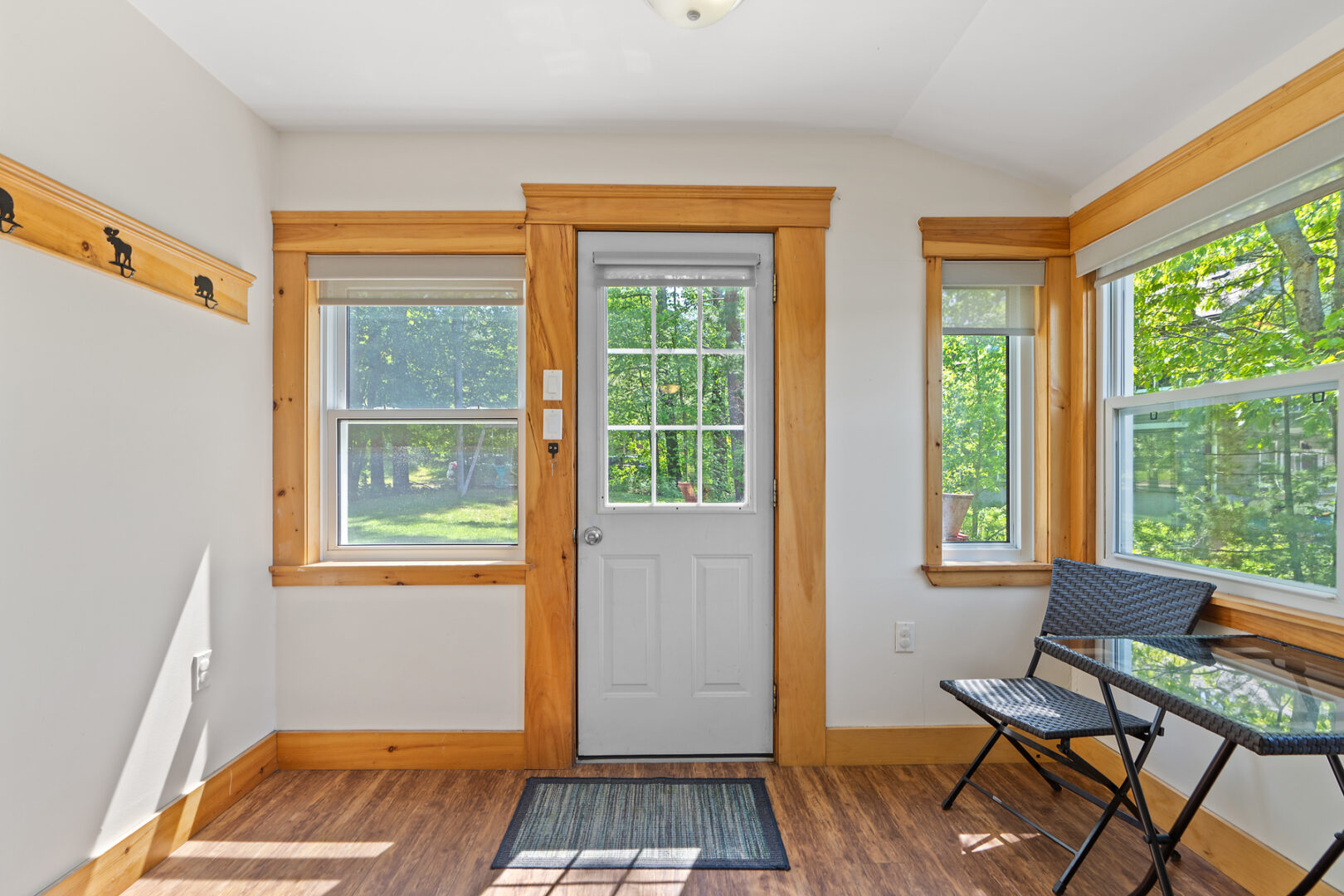Inside the front entrance of a small cottage, with a white front door and walls and hardwood floors.