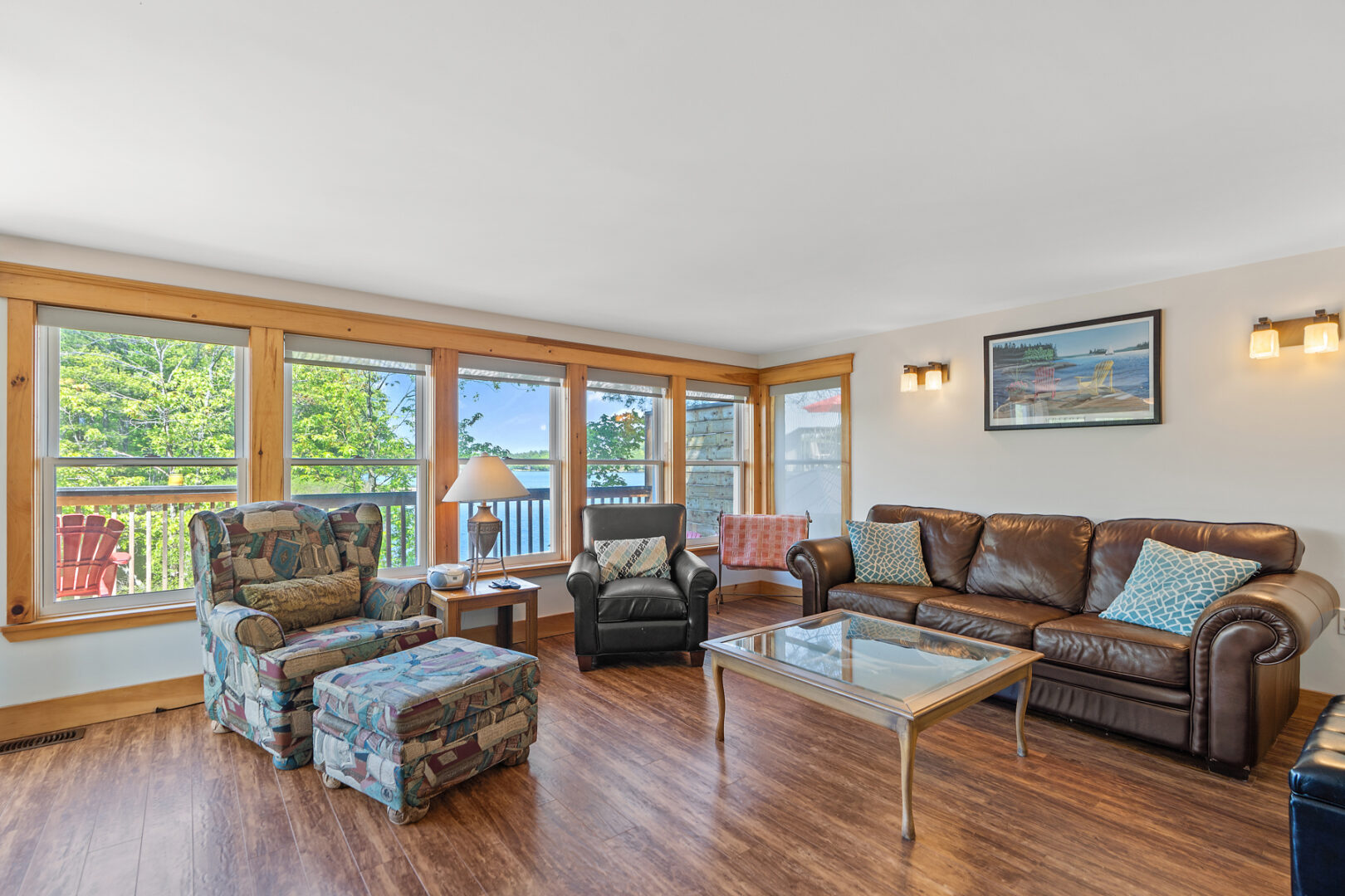 A couch and two chairs sit in front of big windows in a small cottage.