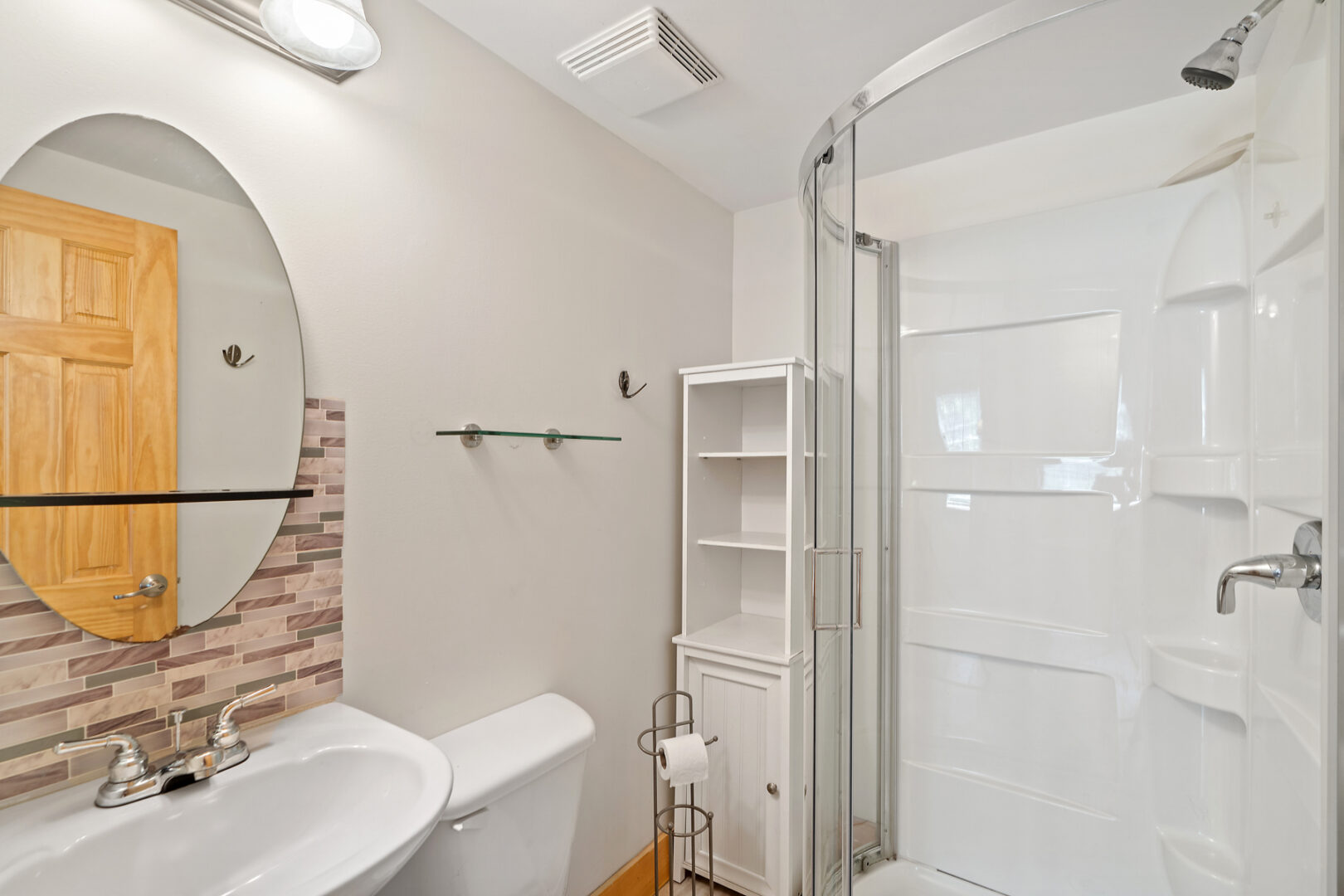 A bright bathroom with a walk-in shower, a toilet, a sink, and a mirror.