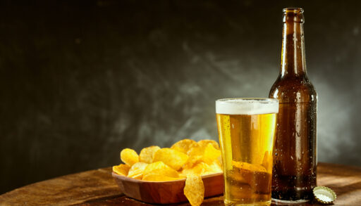 A beer glass and bottle beside a bowl of chips