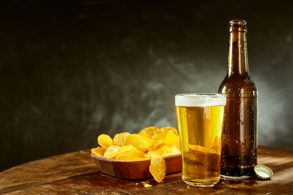 A beer glass and bottle beside a bowl of chips