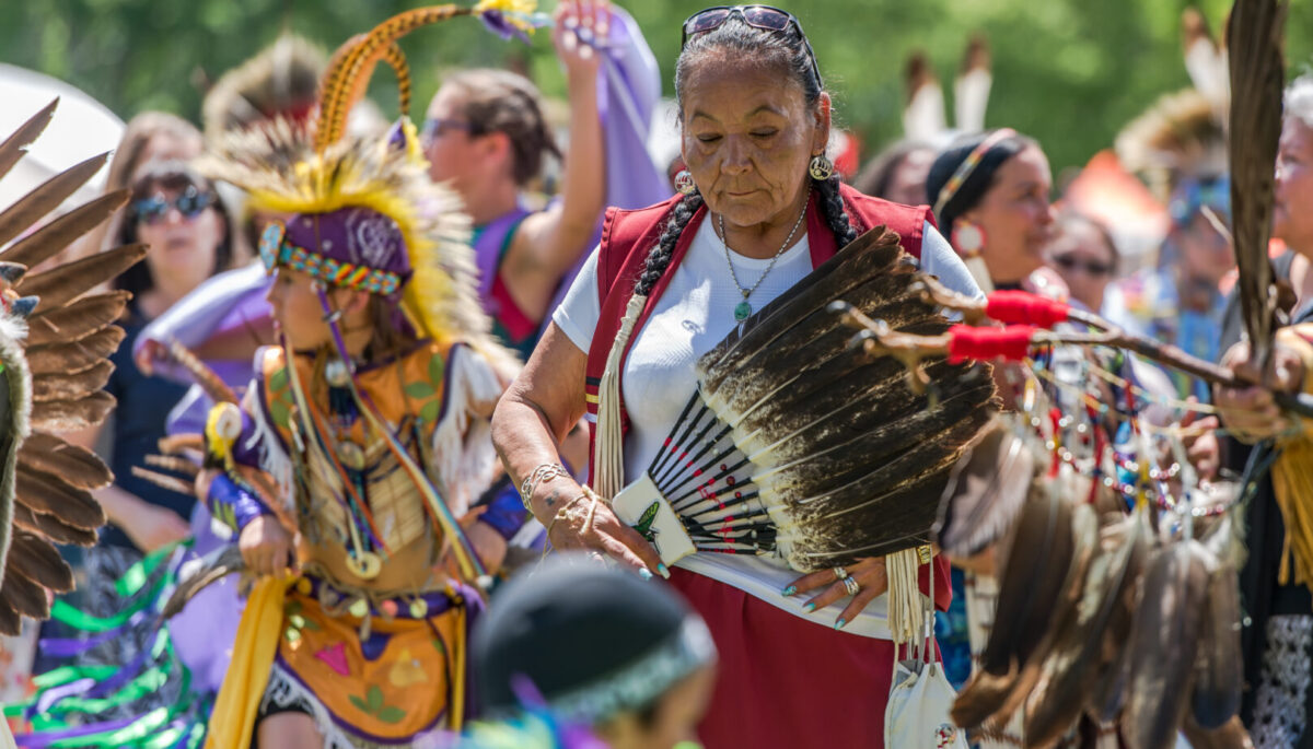 An elder surrounded by youthful and cheerful members of her indigenous community at the 2017 Ottawa Summer Solstice Indigenous Festival at Vincent Massey Park.