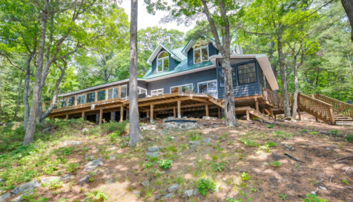 A large cottage sits at the top of a hill in a wooded area.