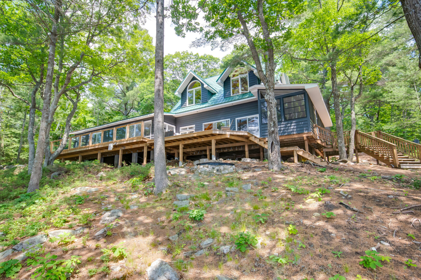 A large cottage sits at the top of a hill in a wooded area.