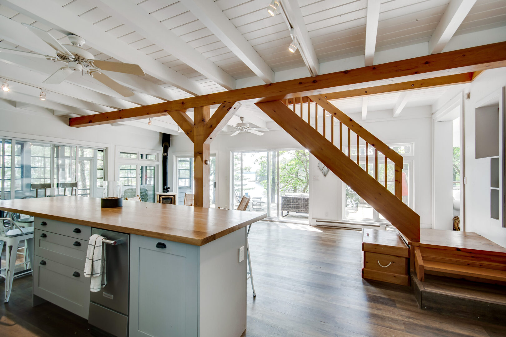 A hardwood staircase leads up to the second floor of a cottage, in the middle of a kitchen and dining area.