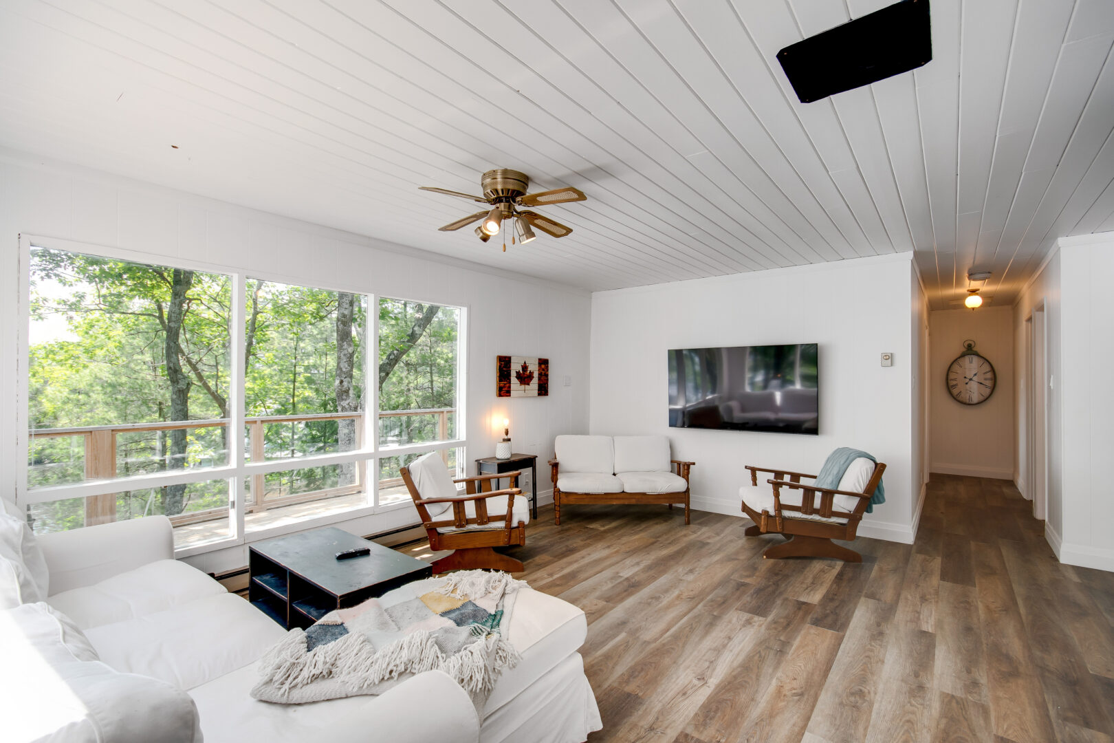 A bright cottage living area with hardwood floors, large windows, and white furniture.