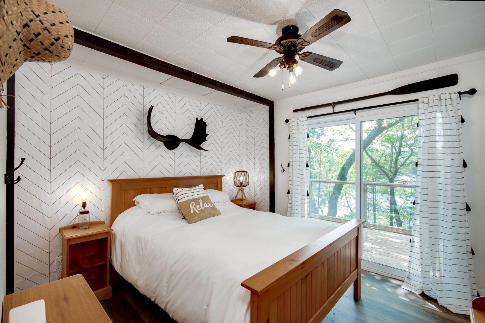 A bright bedroom with a big bed, a ceiling fan, and sliding glass doors leading out to a deck.