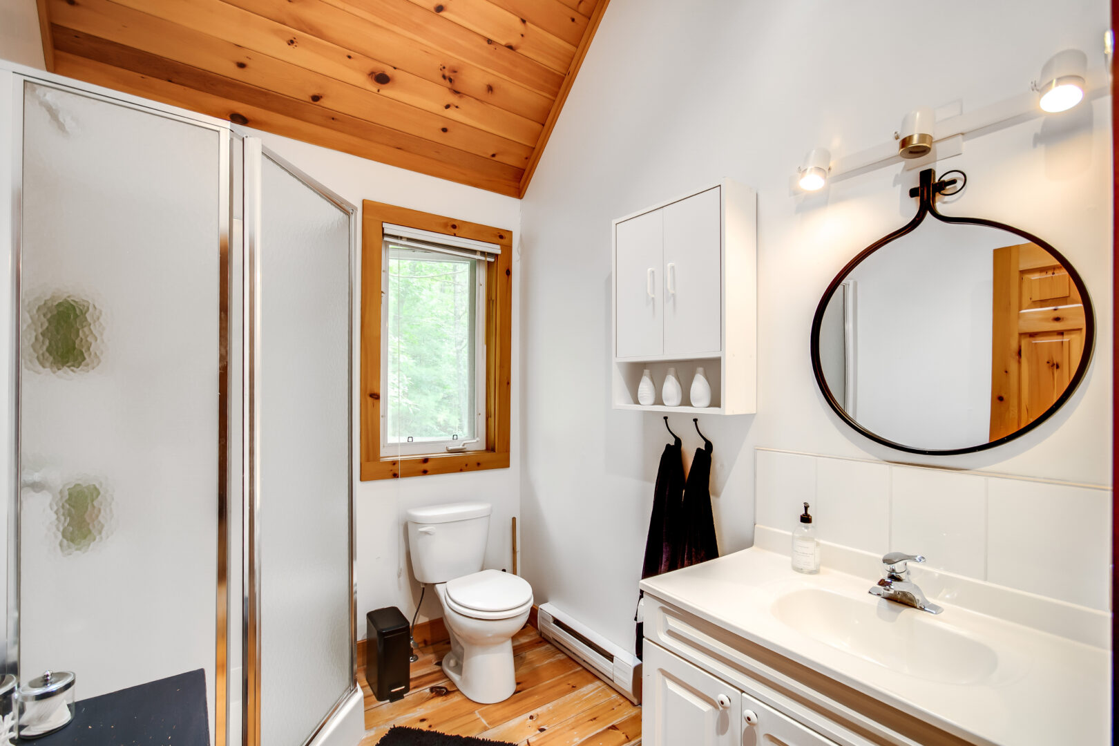 A bathroom with a sloping, wood-panelled ceiling, a walk-in shower, a toilet, and a sink.