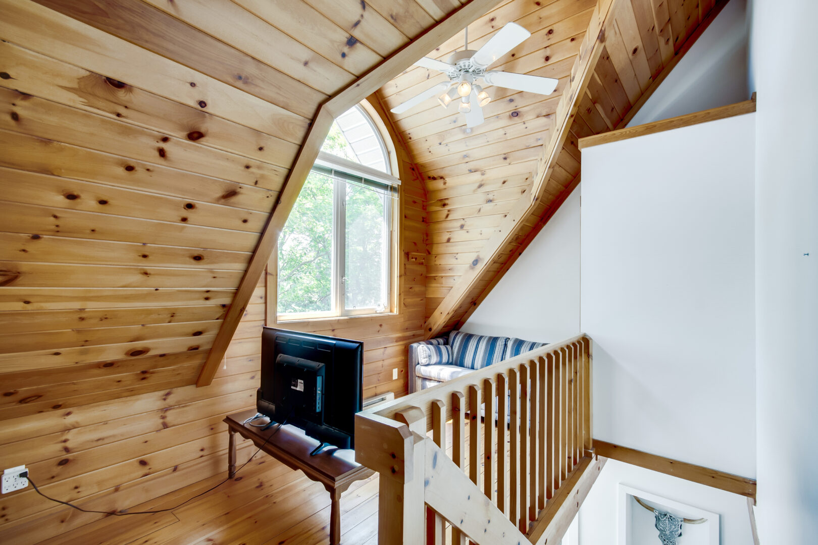 A hallway nook with wood-panelled walls, a small couch and television, and a large window.
