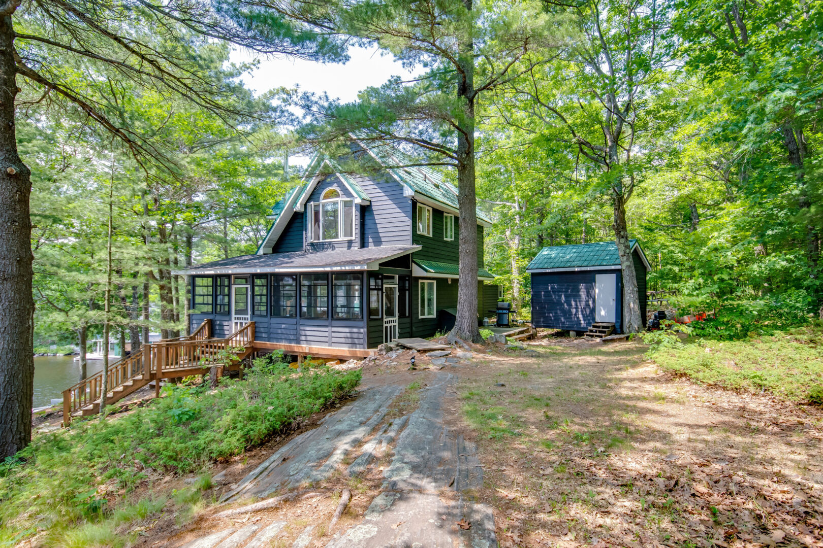 A large cottage and a smaller guest cottage sit side by side, surrounded by trees.