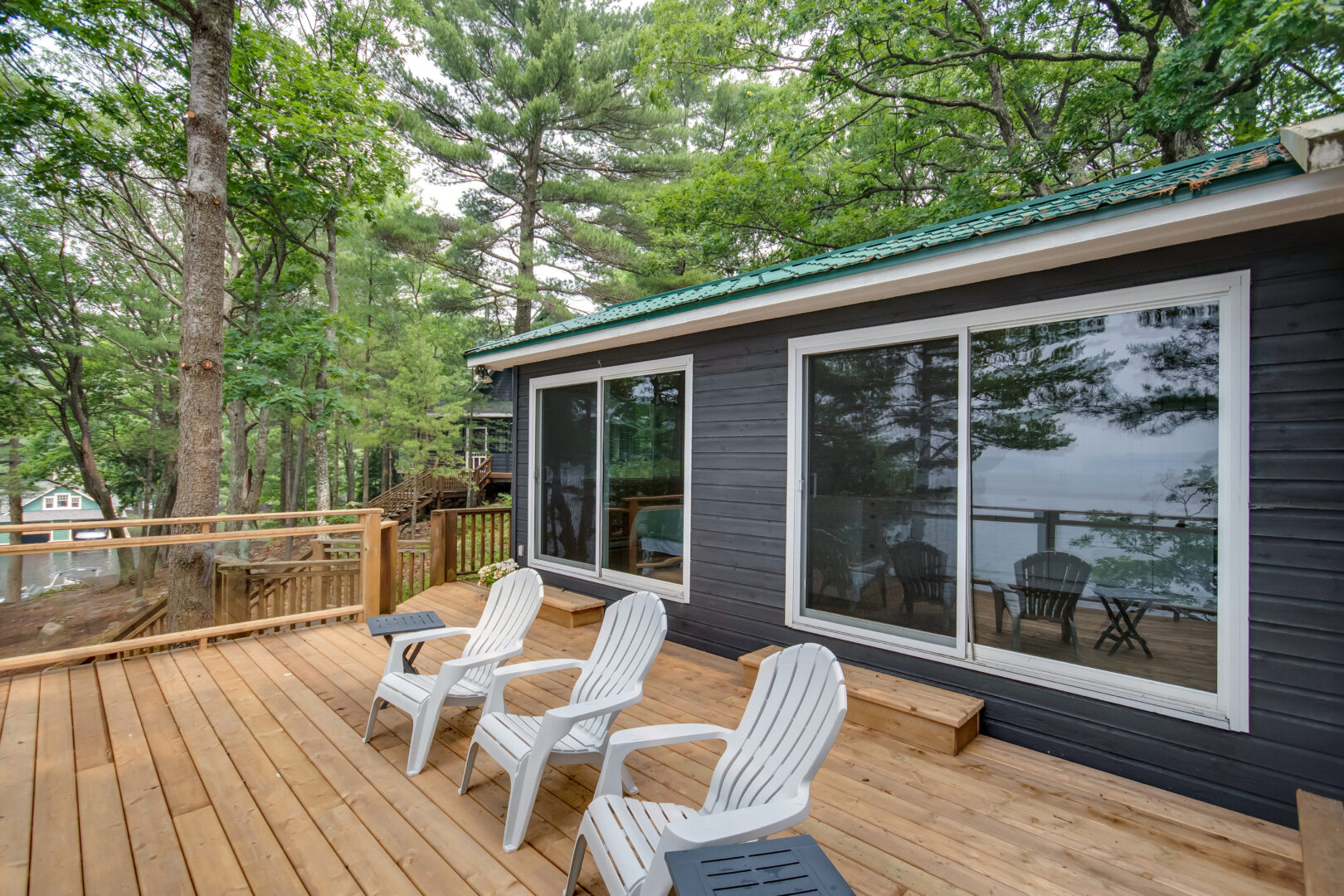 Three chairs sit on a wooden deck, which extends off a guest cabin with large windows.