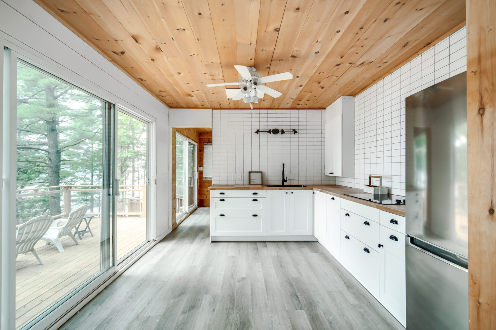 A small but bright kitchen space with gray hardwood floors, white cupboards, and large windows.