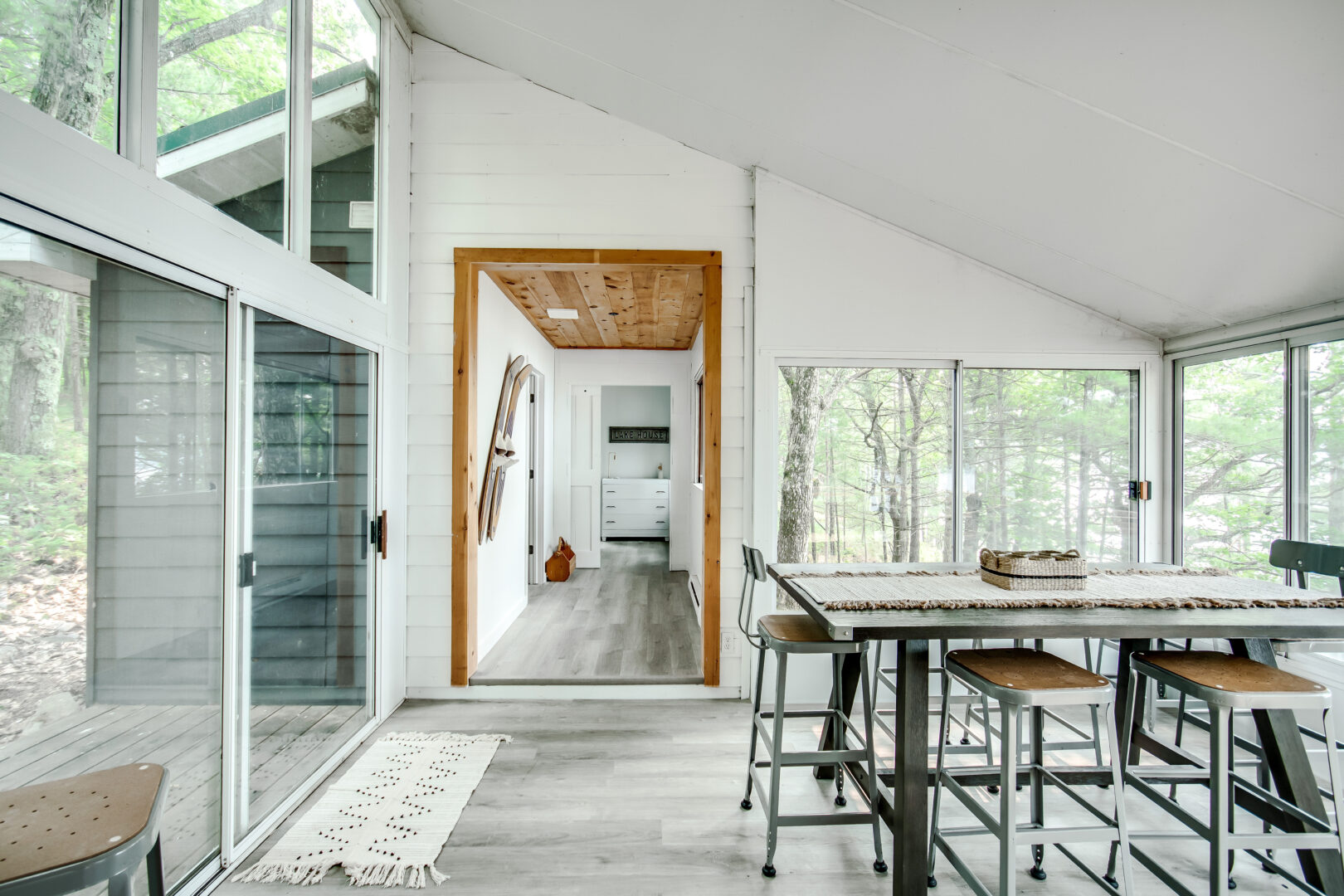 A modern dining area sits in a small but updated guest cabin, which has glass windows lining exterior walls on either side and a sloping ceiling.