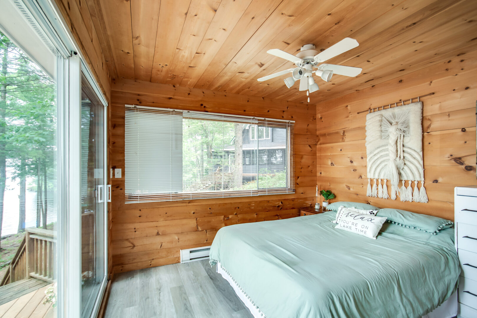 A big bedroom with a wood-panelled ceiling and walls, double glass doors leading outside, and a light blue bedspread.