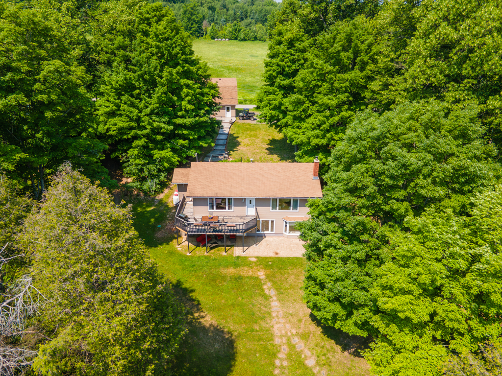 A house sits on a rural waterfront property, surrounded by trees.