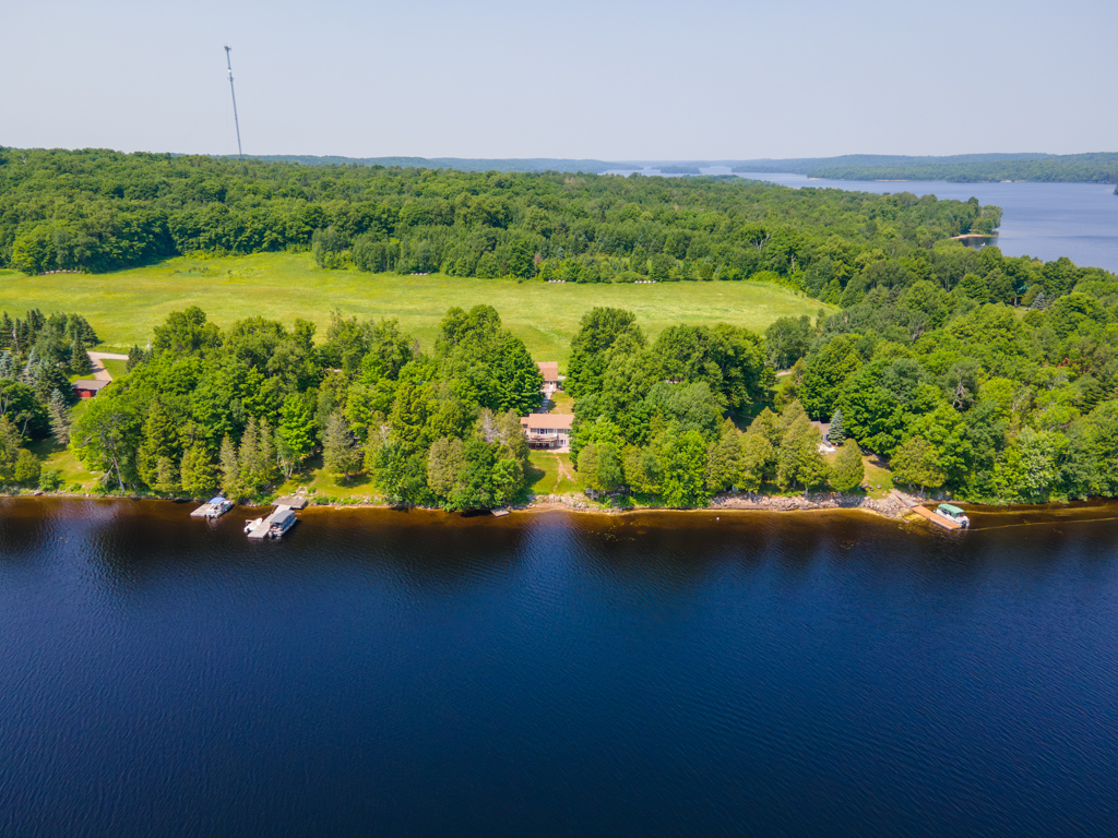A house sits among trees on the shoreline of a deep blue lake.