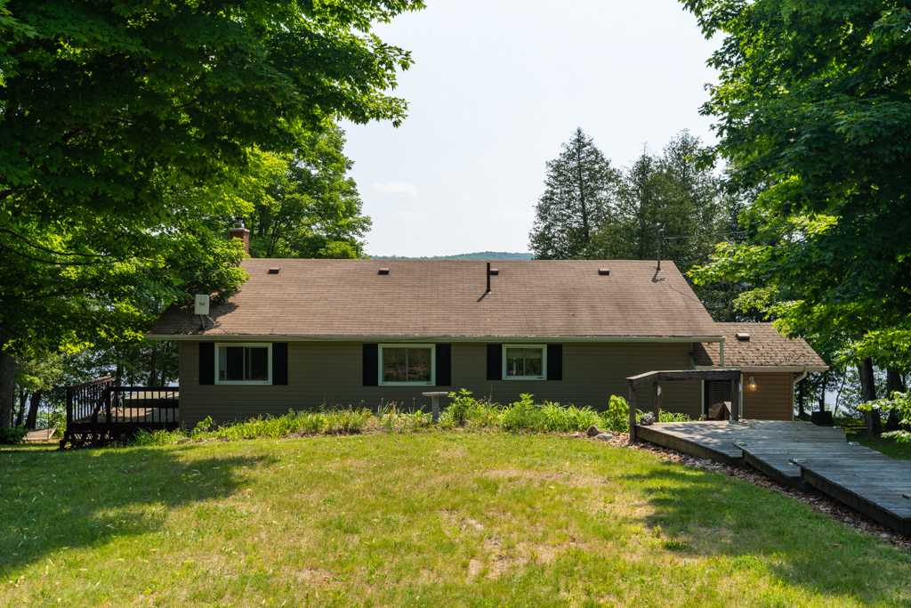A grassy hill leads down to a house with lots of trees on either side.