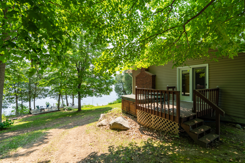 The side of a waterfront home with a small porch and a hot tub. The sloping property leads down to the water.