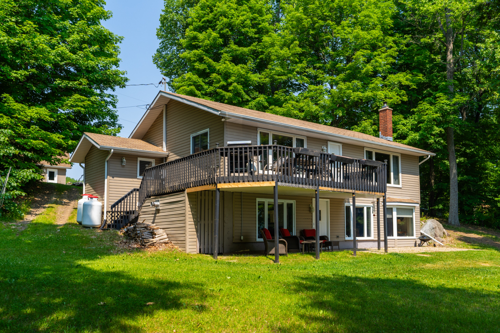 A two-storey house on a grassy hill, with a patio on the ground and a deck extending off the second floor above it.