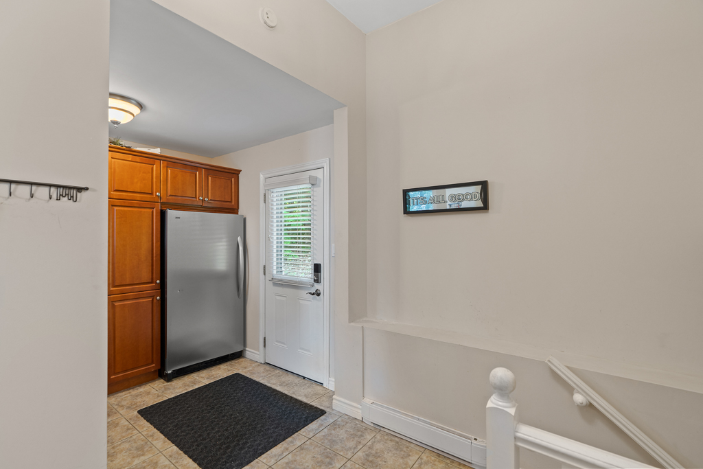 A large fridge beside a front door entrance. Stairs to the other side lead down into the house.