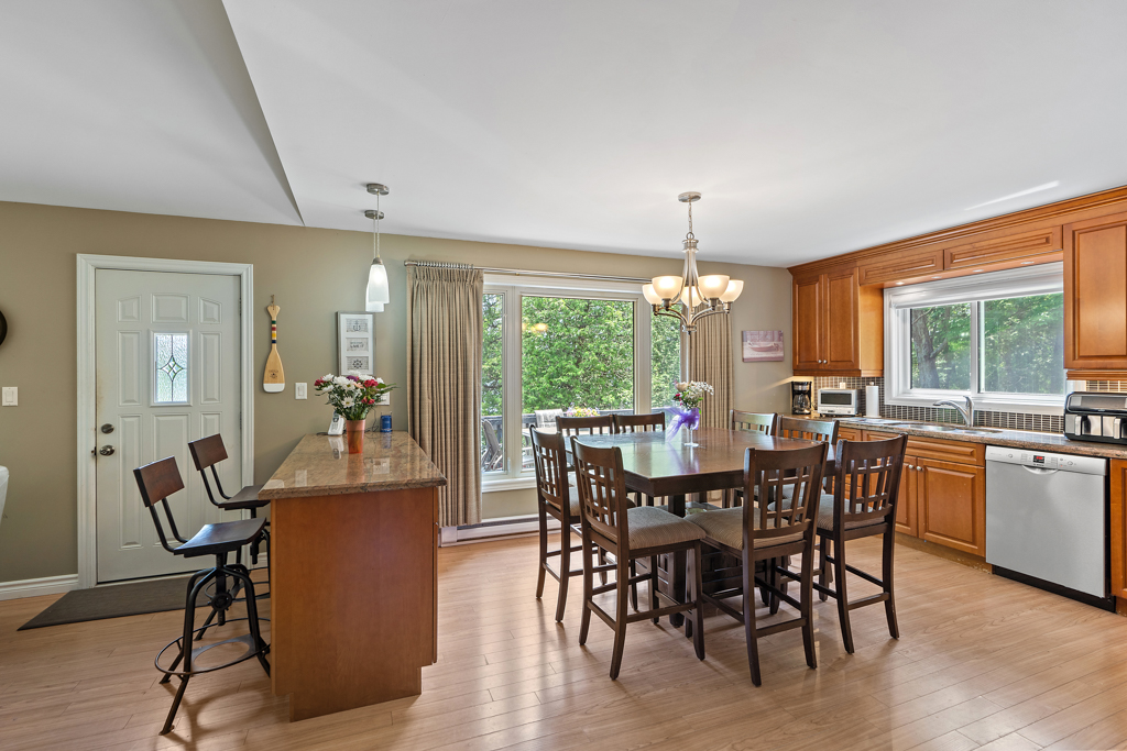A kitchen dining area with a table and chairs, a counter and barstools, hardwood floors, and a large window.