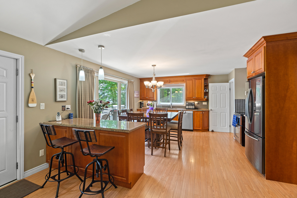 A kitchen dining area with a table and chairs, a counter and barstools, hardwood floors, and a large window.