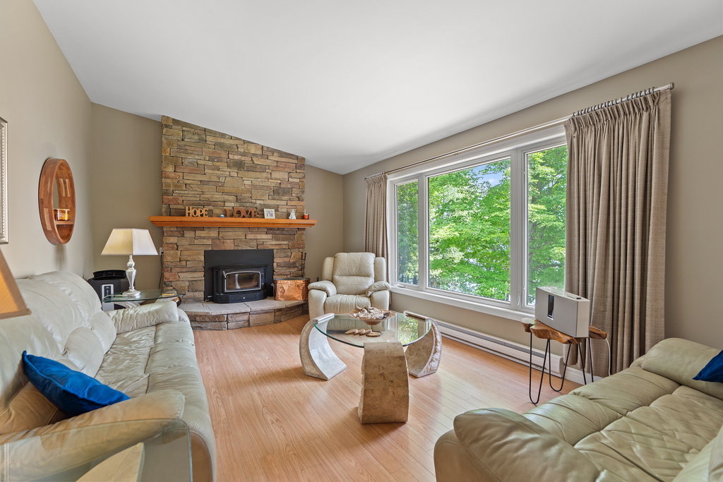 A bright living area with a stone fireplace, white furniture, hardwood floors, and a big window.