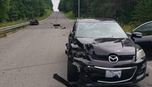 The car involved in the crash with its left side smashed, broken ATV involved in the collision on the left in the background